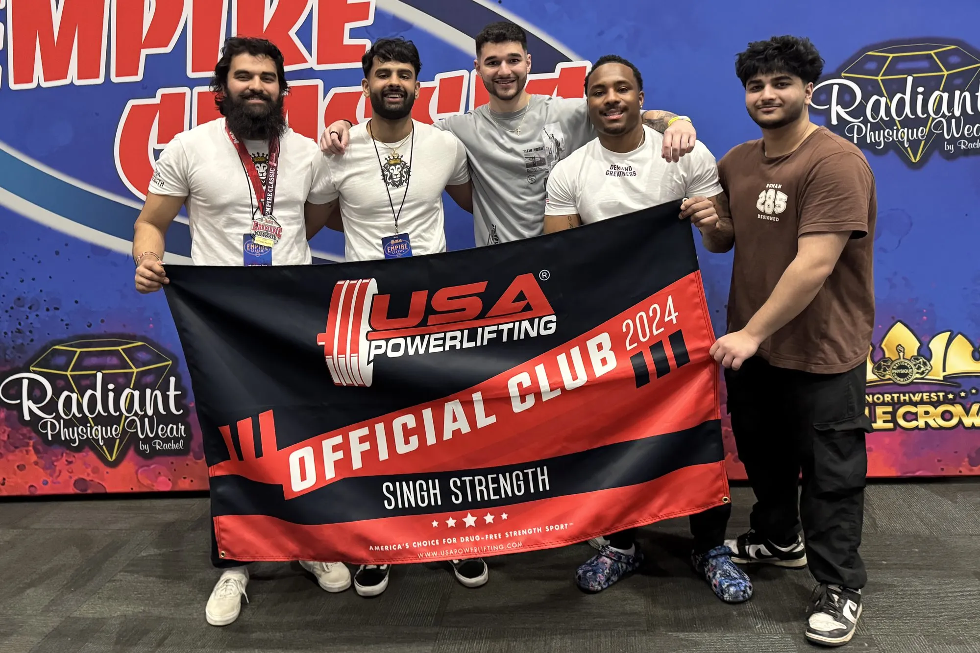 Team Singh Strength holding the USA Powerlifting Official Club 2024 banner at the NPC Empire Classic